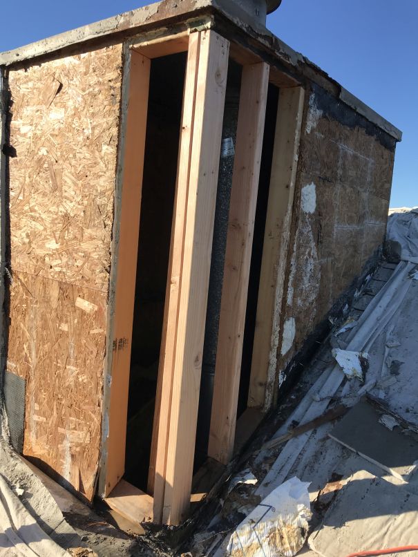 A close-up of a partially constructed wooden structure with exposed beams and plywood, situated on a sloped and weathered roof under a clear blue sky, showcases the early stages before Stucco Services Central Florida are applied.
