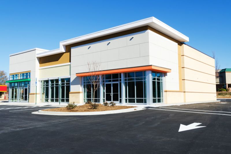 A modern, empty commercial building with large glass windows and doors, featuring quality stucco services. It stands surrounded by a clean, vacant parking lot under a clear blue Central Florida sky.