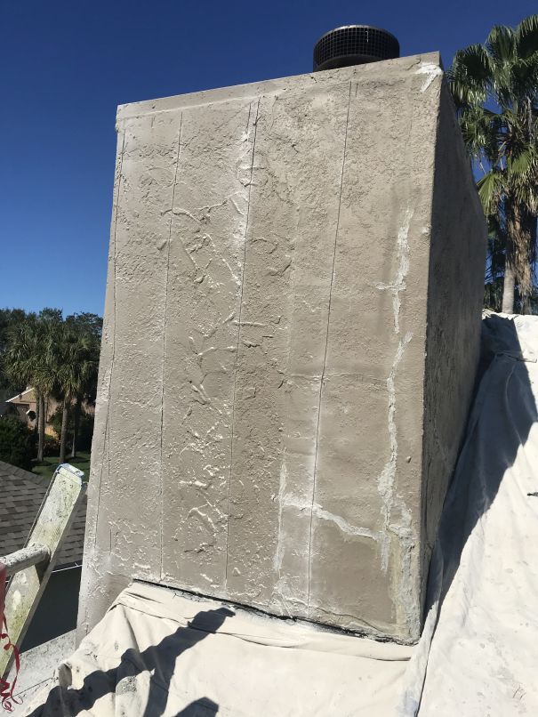 A stuccoed chimney with visible cracks and seams stands on a rooftop, partially covered by a white tarp. Palm trees and a clear blue sky are in the background, hinting at the need for Stucco Services Central Florida can provide.