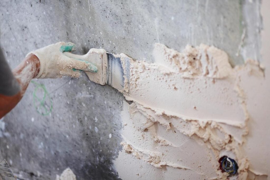 A person wearing a glove is using a trowel to apply plaster or putty to a rough concrete wall, smoothing the surface as part of Stucco Services Central Florida during a construction or renovation project.