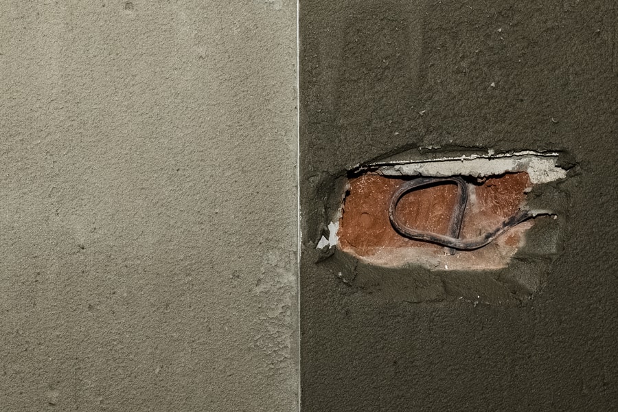 A close-up of a wall with a rough crack exposing red bricks and a black wire, dividing two sections of differently textured plaster—an example often seen before expert repairs by Stucco Services Central Florida.