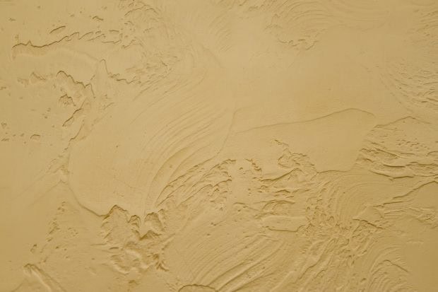 Close-up of a textured beige wall with uneven, swirling patterns and rough, raised areas, showcasing the expert finish provided by Stucco Services Central Florida for a classic stucco-like or plastered appearance.